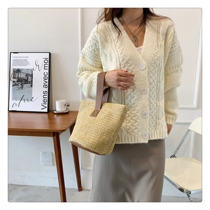 Detail of a woven straw bucket bag with leather handles paired with a knit cardigan