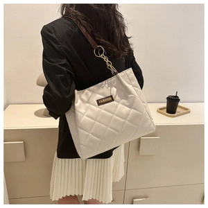 Model wearing a white quilted tote bag with chain strap in a cozy indoor setting