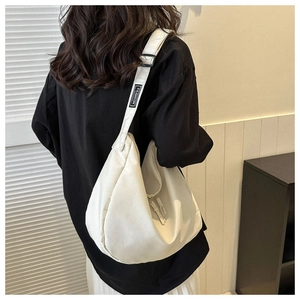 Détail du sac bandoulière demi-lune blanc cassé avec étiquette FASHION sur la sangle