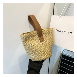 Close-up of woven straw bucket bag featuring reinforced brown leather handles and neat texture
