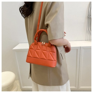 Detail of orange quilted handbag showing geometric stitching and gold-tone zippers