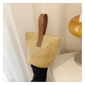 Detail of minimalist straw tote bag with brown leather handle and cross-stitch reinforced seam