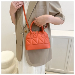 Chic orange quilted dome crossbody bag styled with a light brown blazer and white outfit