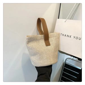 Detailed view of woven straw bucket bag with brown leather handle and texture