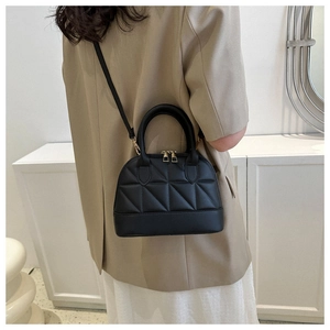 Close-up of quilted black leather shell bag with gold hardware worn by model