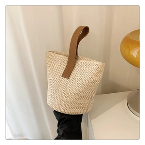 Detail of straw woven bucket bag with brown leather handles on a minimalist table