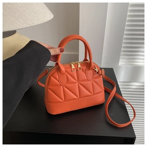 Detail of orange quilted shell handbag with gold zippers on a black table setting