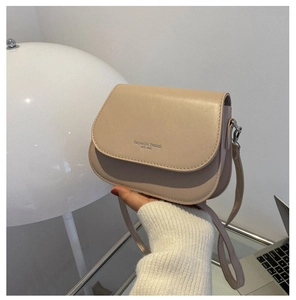 Close-up of beige saddle bag with silver lettering and adjustable thin shoulder strap