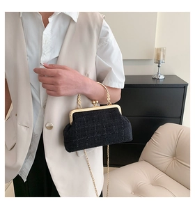 Detail of black tweed woven bag with vintage gold metal handle and chain strap on person