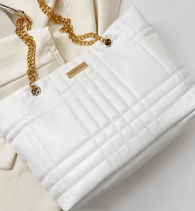 Detail showing white quilted leather texture and gold chain strap of the shoulder bag