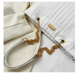 Detail of white quilted faux leather bag featuring golden chain strap and padded shoulder