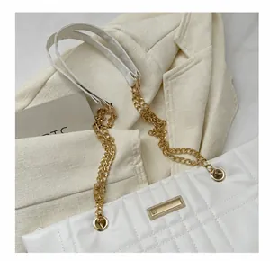 Detail of white quilted handbag featuring gold hardware and leather chain strap