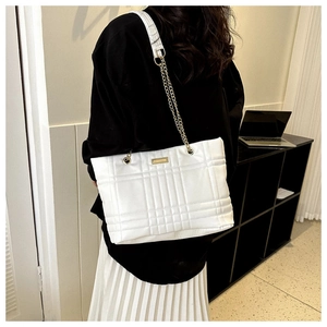 Detail of white quilted tote bag with golden chain strap and rectangular metal logo plate
