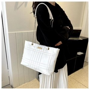 Detail of white quilted tote bag featuring gold chain strap and elegant lattice texture