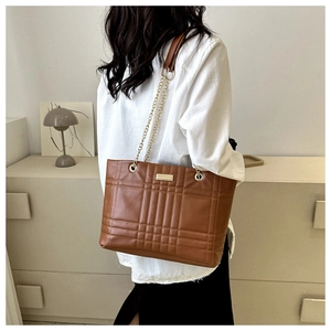 Close-up of brown quilted leather tote bag with elegant gold chain strap detail on shoulder