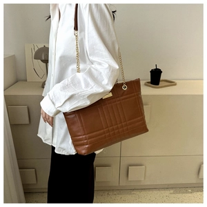 Caramel brown quilted tote bag with gold chain strap shown on model in studio