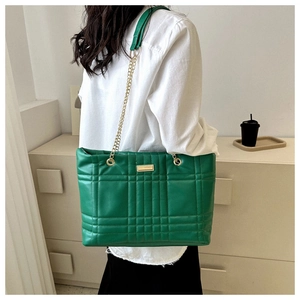 Detail of green quilted tote bag with gold chain strap and metal plate ornament
