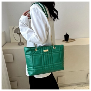 Detail of green quilted tote bag featuring golden chain straps and elegant metal plate