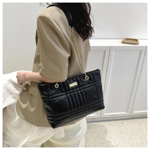 Detailed view of black quilted tote bag with gold chain strap worn by a stylish model