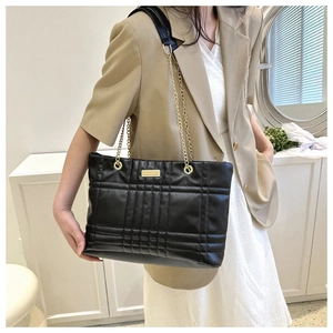 Close-up of quilted black leather tote with gold chain strap and metal logo plaque