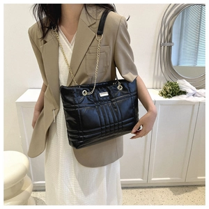 Quilted black tote bag with gold chain strap shown on model in a minimalist room