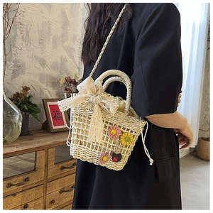 Beige hand-woven bag with large lace bow and colorful floral details on a black outfit