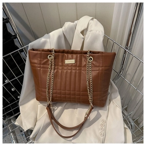 Detail of a brown quilted tote bag with gold chain strap on a white blazer