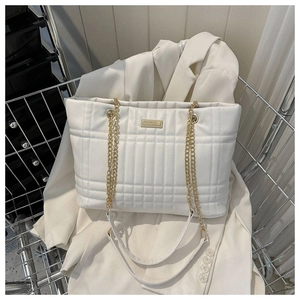 Close-up of white quilted tote bag with golden chain strap and metallic logo plate