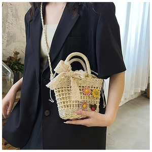 Detail of hand-woven beige straw bucket bag with floral daisy decor and lace bow