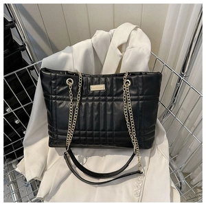 Detail of black quilted puffer tote bag with gold chain strap on white blazer