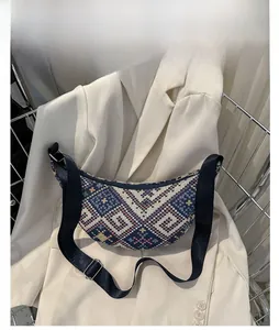 Détail du sac croissant tissé bleu à motifs géométriques sur un blazer blanc