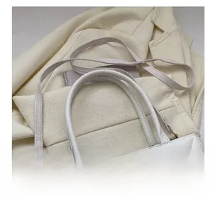 Close-up of white quilted crossbody bag with adjustable strap on beige blazer