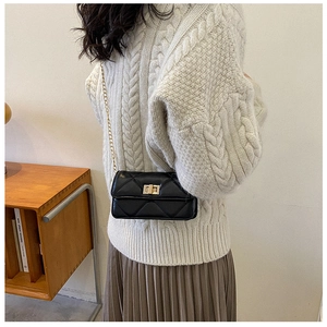 Detail of black quilted chain strap bag styled with a white knit sweater and brown skirt