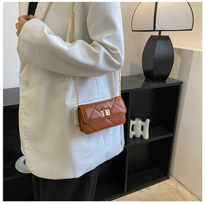 Close-up of a brown quilted leather crossbody bag with a gold lock on a white suit