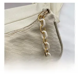 Macro shot of stylish gold metal and white resin chain links on a beige shoulder bag