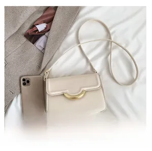 Detail view of cream shoulder bag with horseshoe metal buckle showing phone size comparison