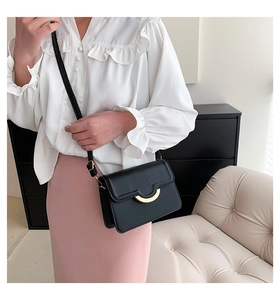 On-body shot of a minimalist black leather crossbody bag with a gold semi-circle clasp
