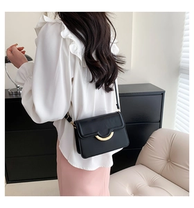 Detail of a black crossbody bag with a golden semicircular clasp worn by a model