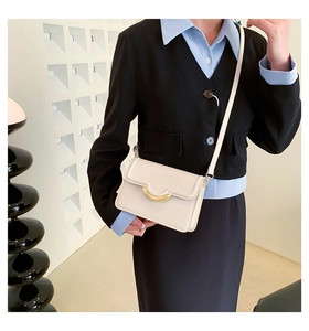 Detail of cream rectangle crossbody bag with gold semi-circular buckle on a model