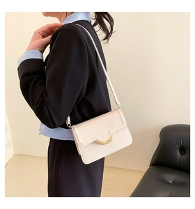 Close-up of a cream crossbody bag with a gold semi-circle buckle on a model
