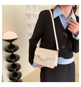 Detail of cream leather crossbody bag featuring a signature golden semicircular metal buckle