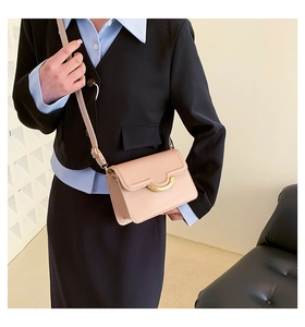 Detail of a minimalist square crossbody bag with a distinctive gold semicircular metal clasp