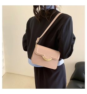 Detailed back view of a beige crossbody bag featuring a distinctive gold semicircular clasp