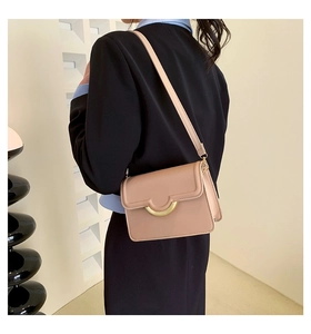 Close-up of minimalist beige crossbody bag with a semi-circular gold metal buckle detail