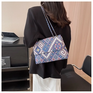 Detail view of a blue woven shoulder bag with geometric patterns and a gold chain strap