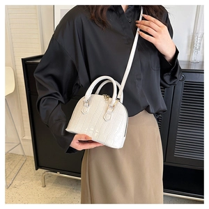 Detail shot of a white crocodile pattern shell bag held by a model in a minimalist setting