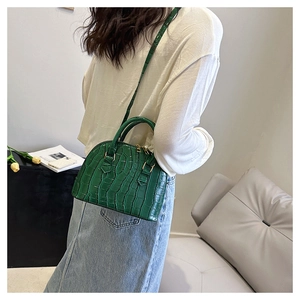 Detail view of dark green croc-embossed shell bag with gold zippers and slim strap