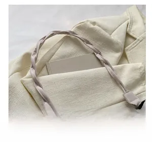 Detail of cream crossbody bag featuring a wide woven strap and elegant pearl charm detail