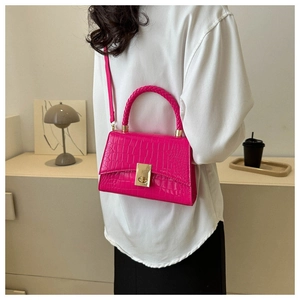 Detailed view of rose red crocodile pattern handbag with gold clasp on a shoulder strap