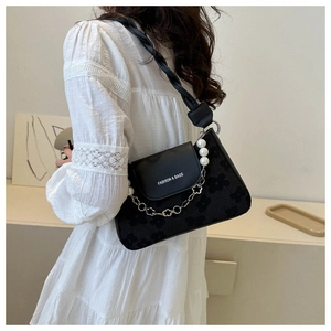 Detail of black textured shoulder bag featuring pearl chain and letter print on flap